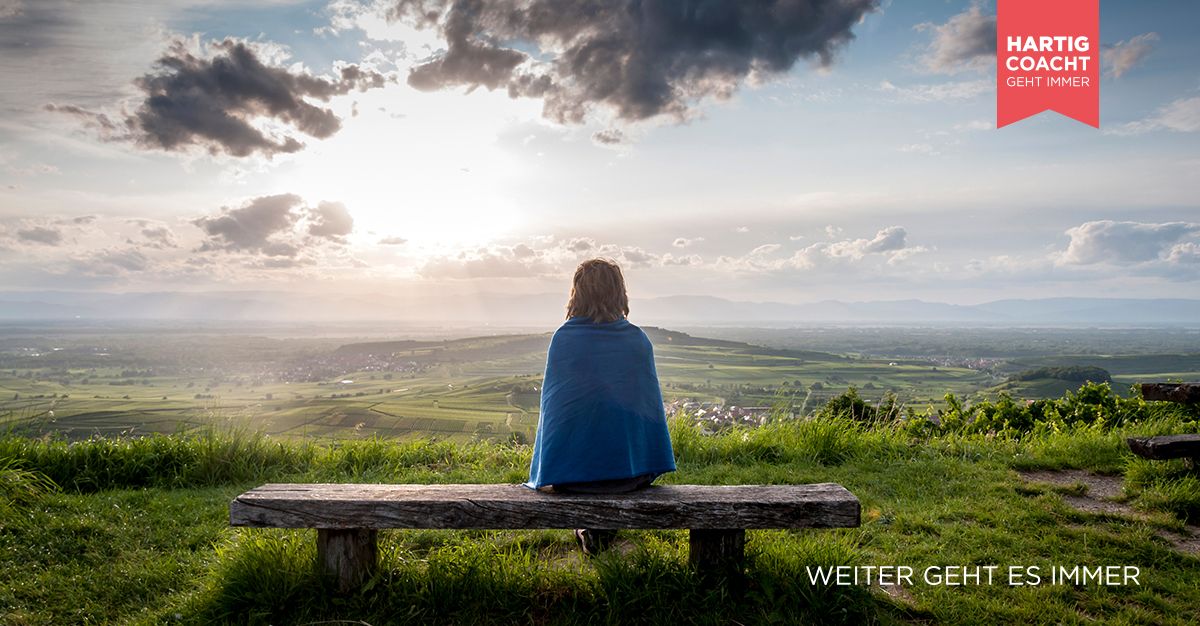 Frau sitzt auf einer Bank und schaut in eine weite Landschaft