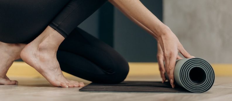 Frau barfuß rollt eine Yogamatte aus